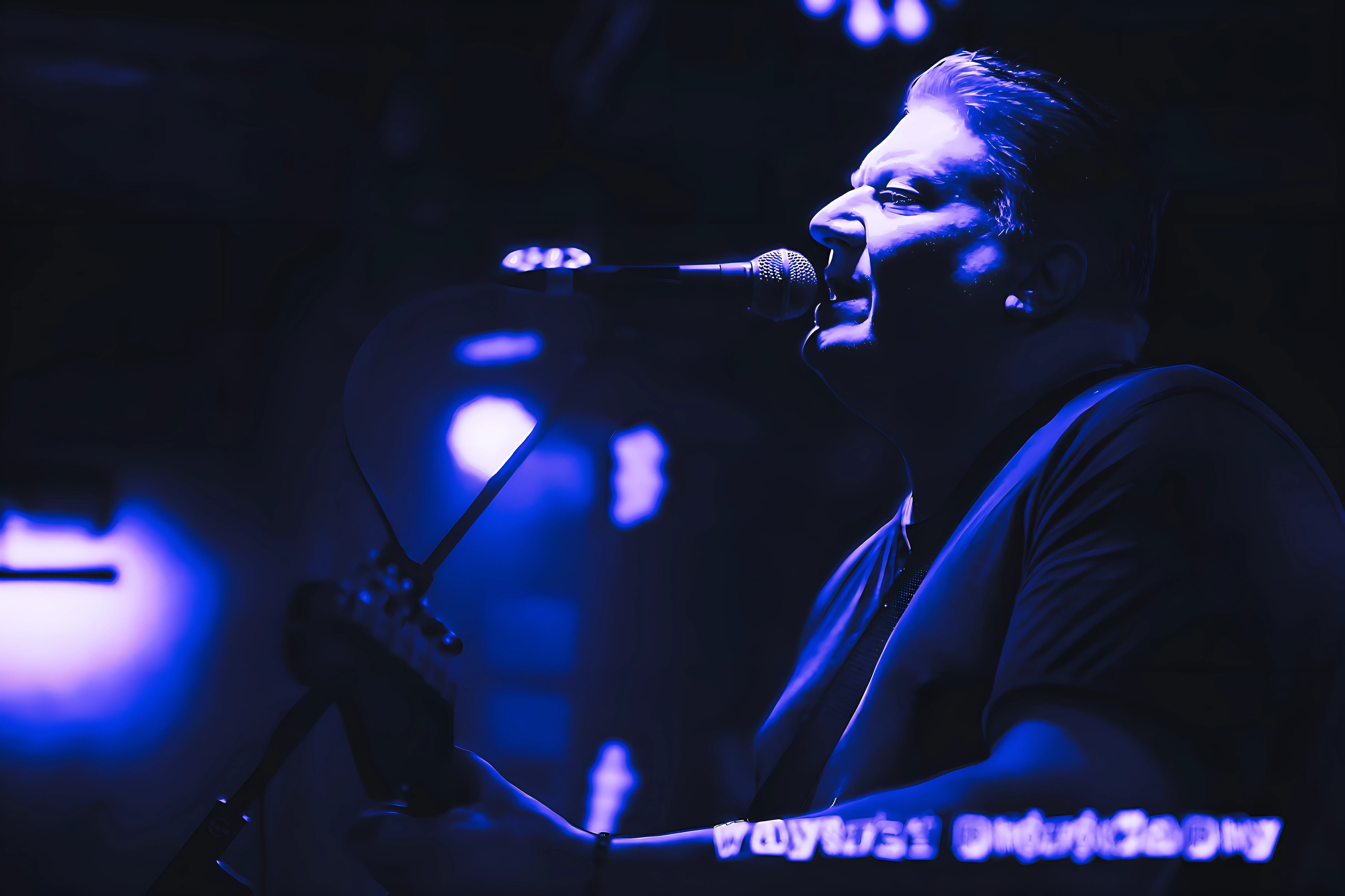 Mike Breen at the microphone, stage light cast in deep blue, Whistle Binkies Edinburgh